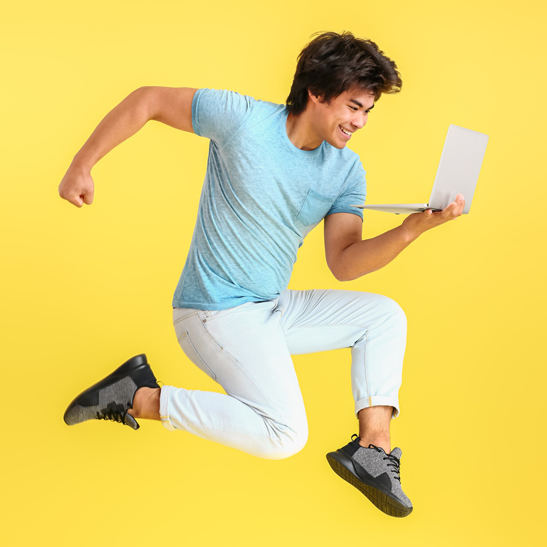 Jumping Male Asian Programmer with Laptop on Color Background